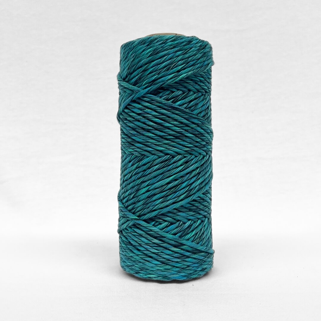 one roll of 4mm cotton mixed string in colourway aura blue a combination of blue green and black standing upright on white backdrop