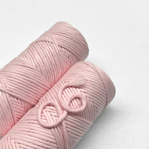 two rolls of pastel pink cotton cord for macrame and weaving laying flat on white background