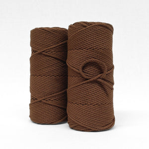 two rolls of chocolate brown braided cord standing upright o white backdrop