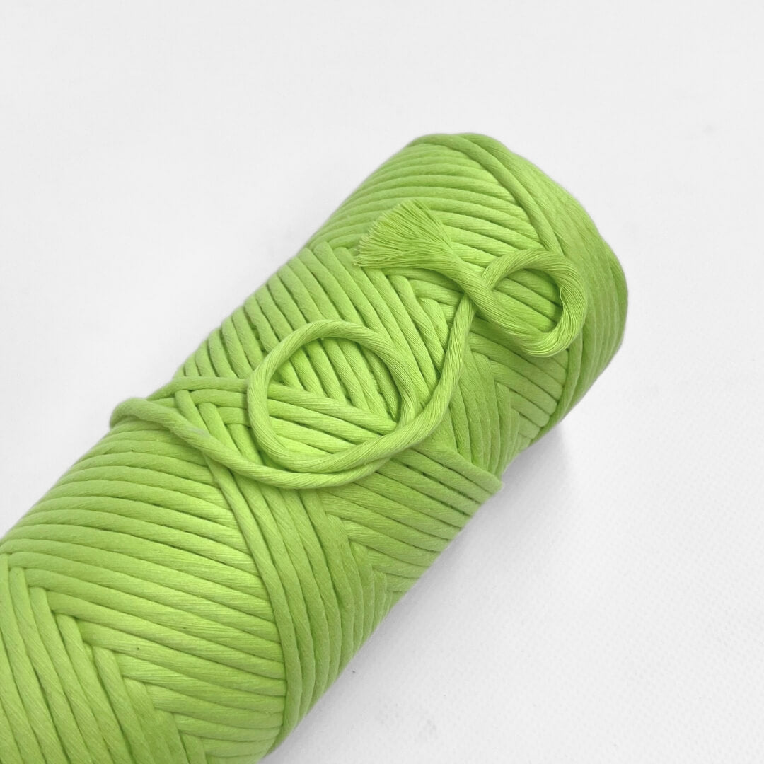 roll of neon green cotton macrame string laying lat on white background