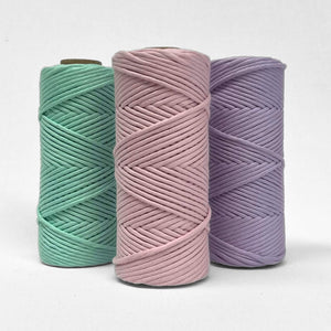 three rolls of macrame cord in spring green frosted pink and pastel purple standing in triangle formation on white background