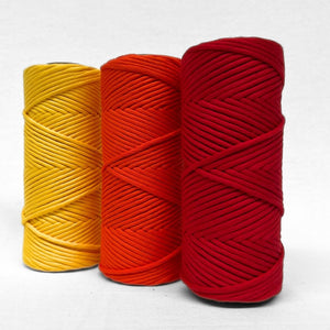 three rolls of premium cotton string in daffodil yellow flame orange and ladybug deep red standing side by side on angle on white background