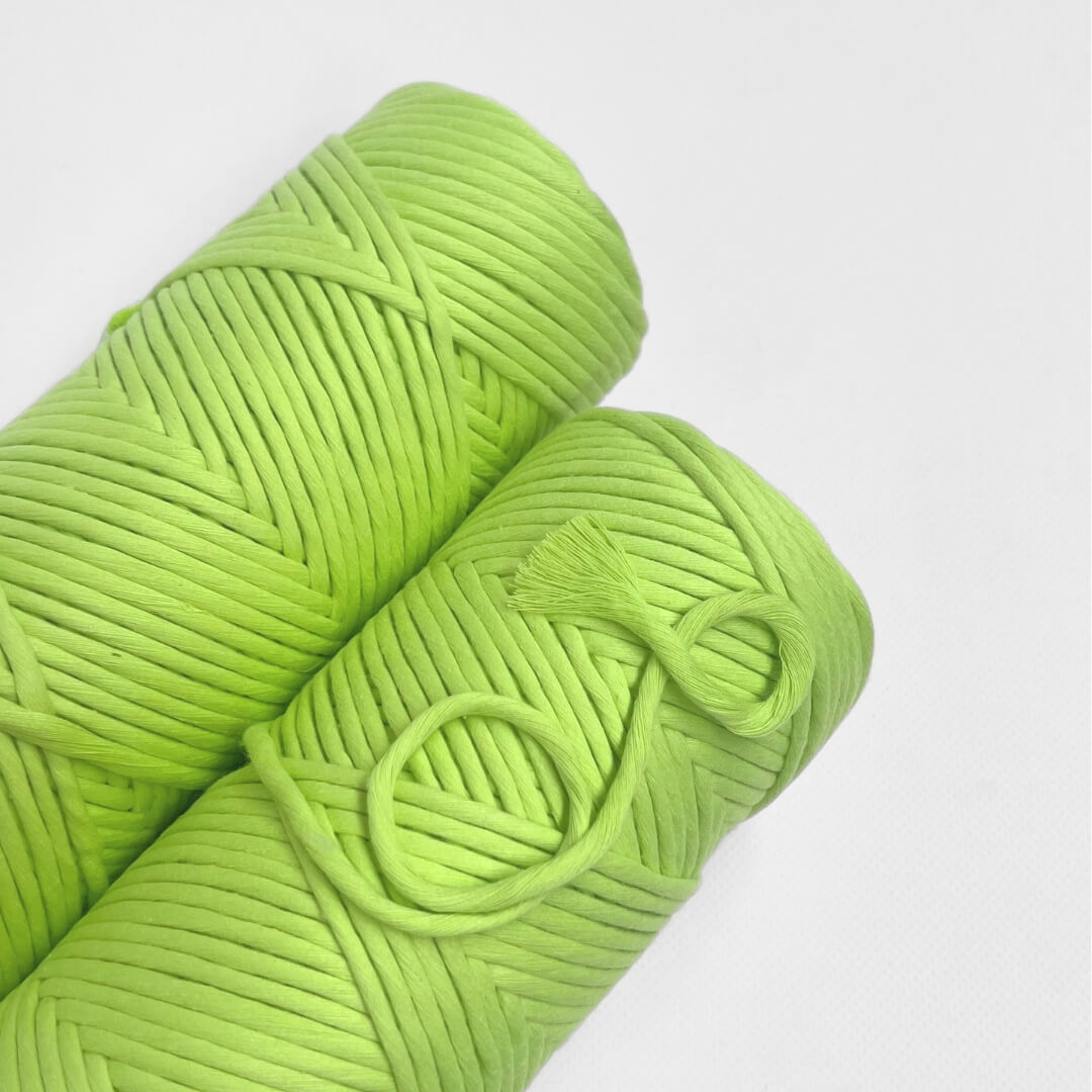 roll of neon green cotton macrame string laying lat on white background