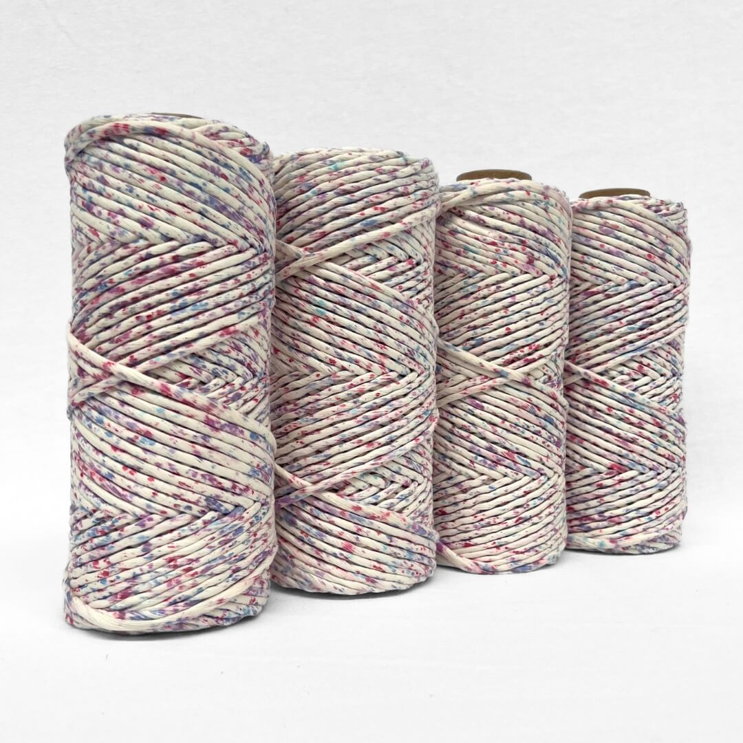 four rolls of pink purple and blue specklied cotton string standing side by side on white background