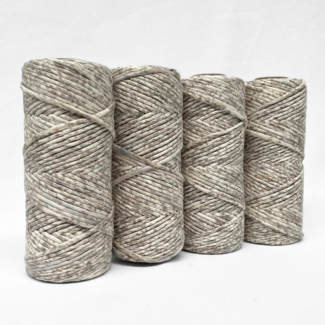 four standing rolls of neutral browns speckled cotton string showing slight variation between each roll on white back ground 
