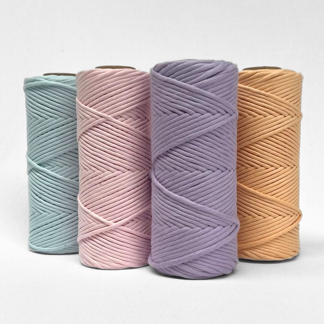 four rolls of macrame cord in blue pink purple and orange stnading upright on white background 