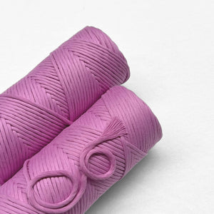 two rolls of vivid violet cotton cord laying flat side by side on white backdrop