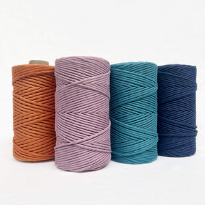 bright orange purple vibrant blue deep blue macrame cotton string four rolls standing up in combination photo on white wall
