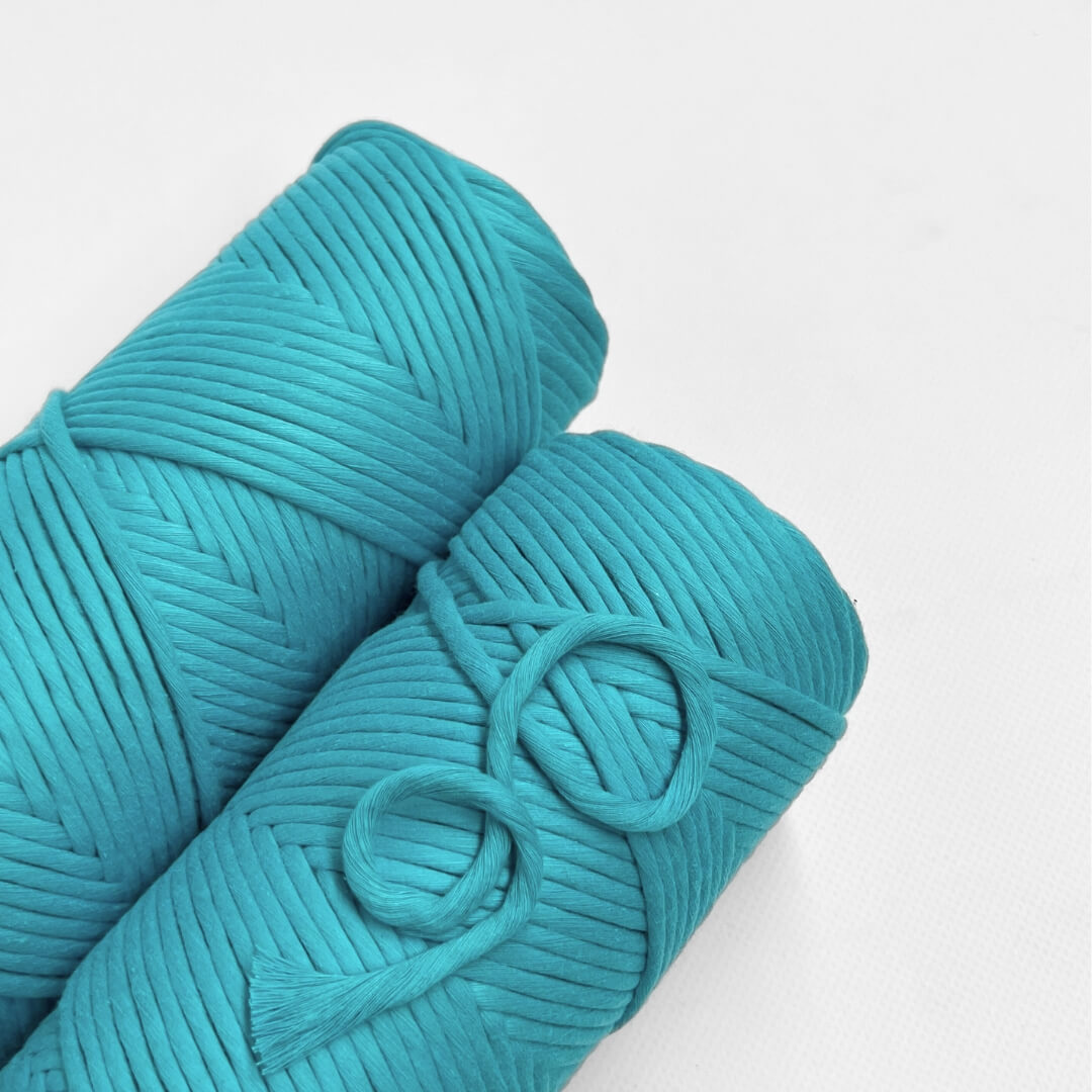 single roll of ocean blue macrame string laying on white background