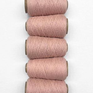 Soft blush pink thin wool yarn 5 angular rolls laying side by side from top to bottom on white background