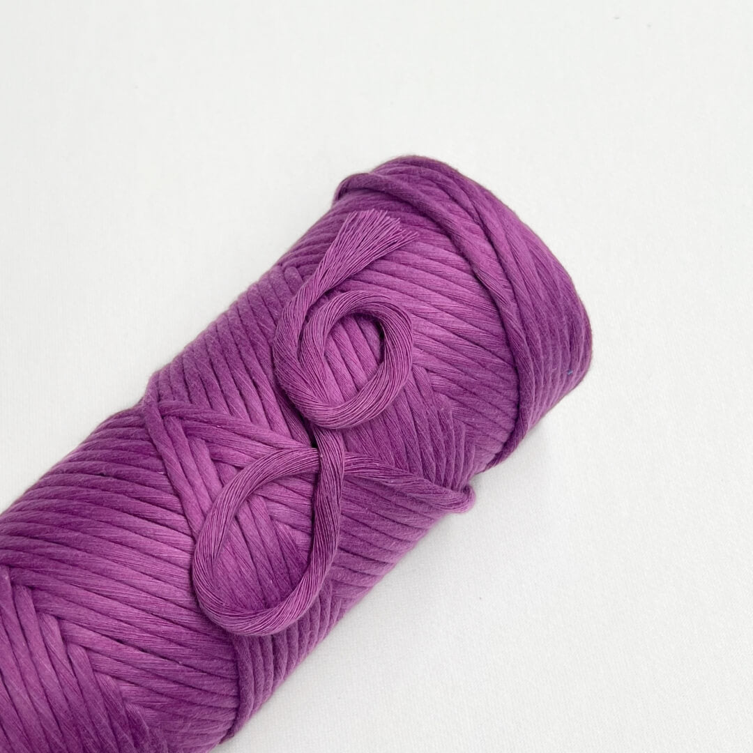 one roll of macrame cotton string laying angled and flat in colour royal purple on white background