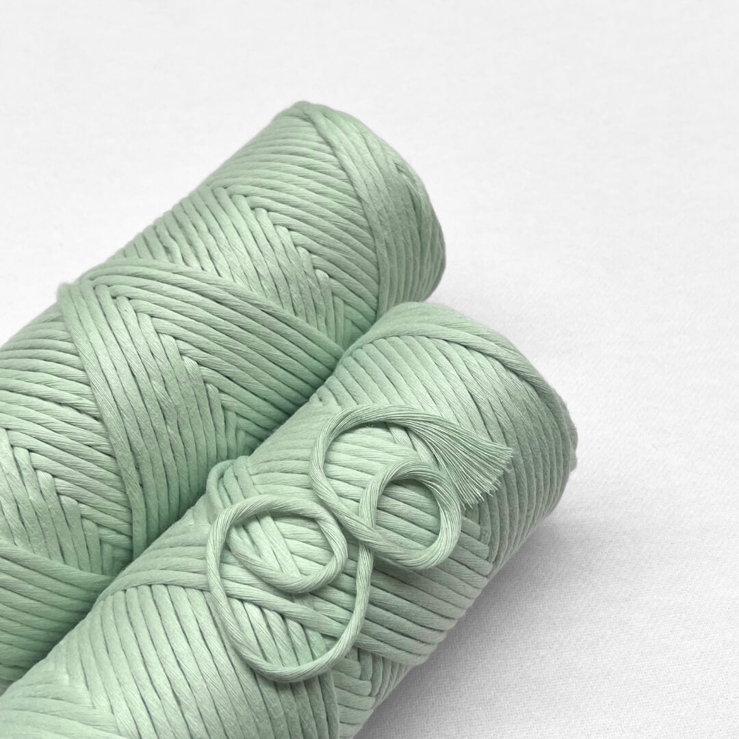 two rolls of mint green cotton macrame string laying flat on white background 