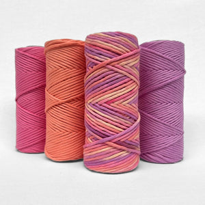 one roll of pink purple yellow hand painted string next to three matching colours of cotton string on white background