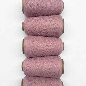 Five rolls of primrose pink wool yarn side by side in flat lay on white background 