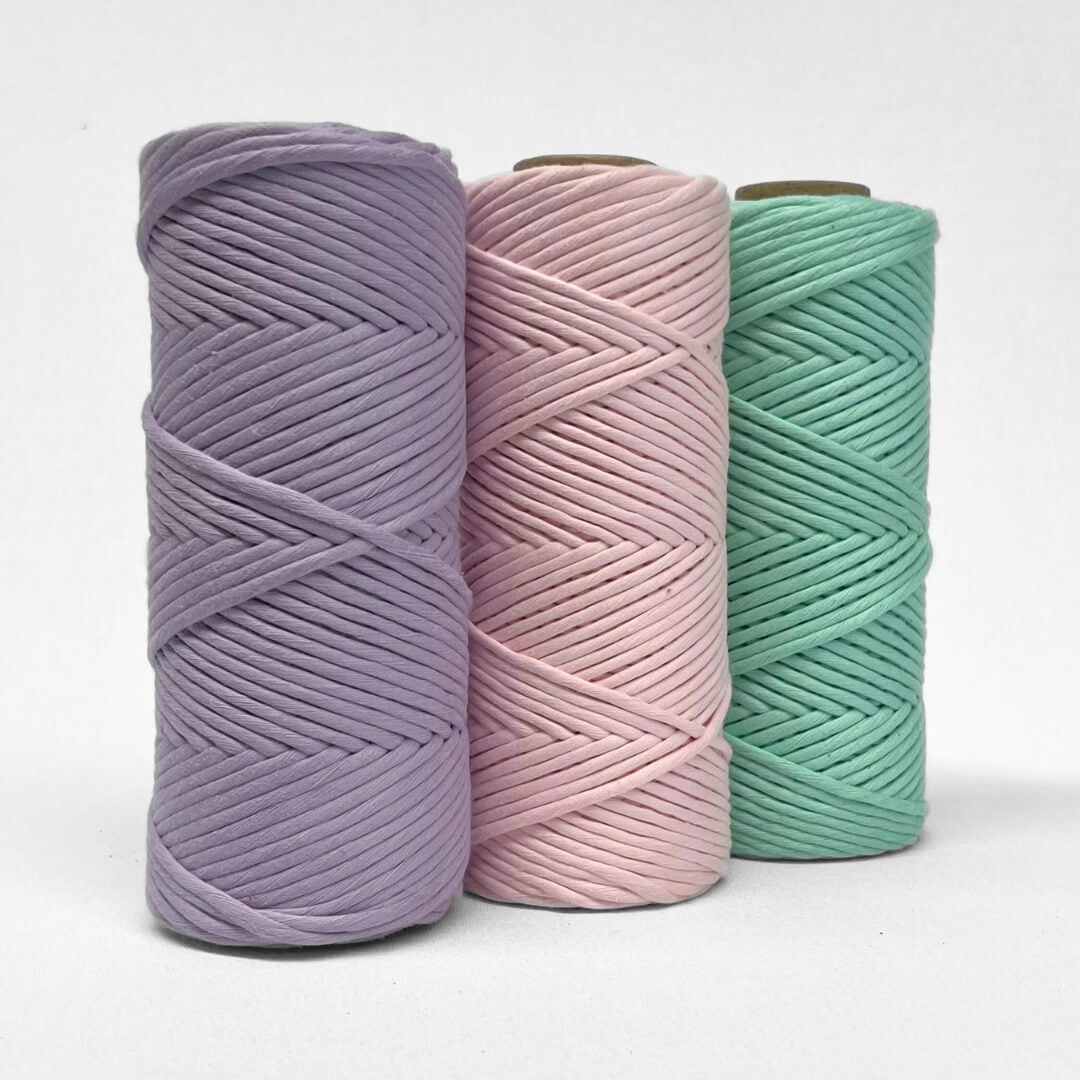 three rolls of macrame cord in purple pink and mint green colour way standing upright with white background 