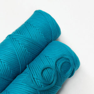 two rolls of barrier reef blue macrame string laying flat on white wall small curled and brushed piece showing up close texture of product