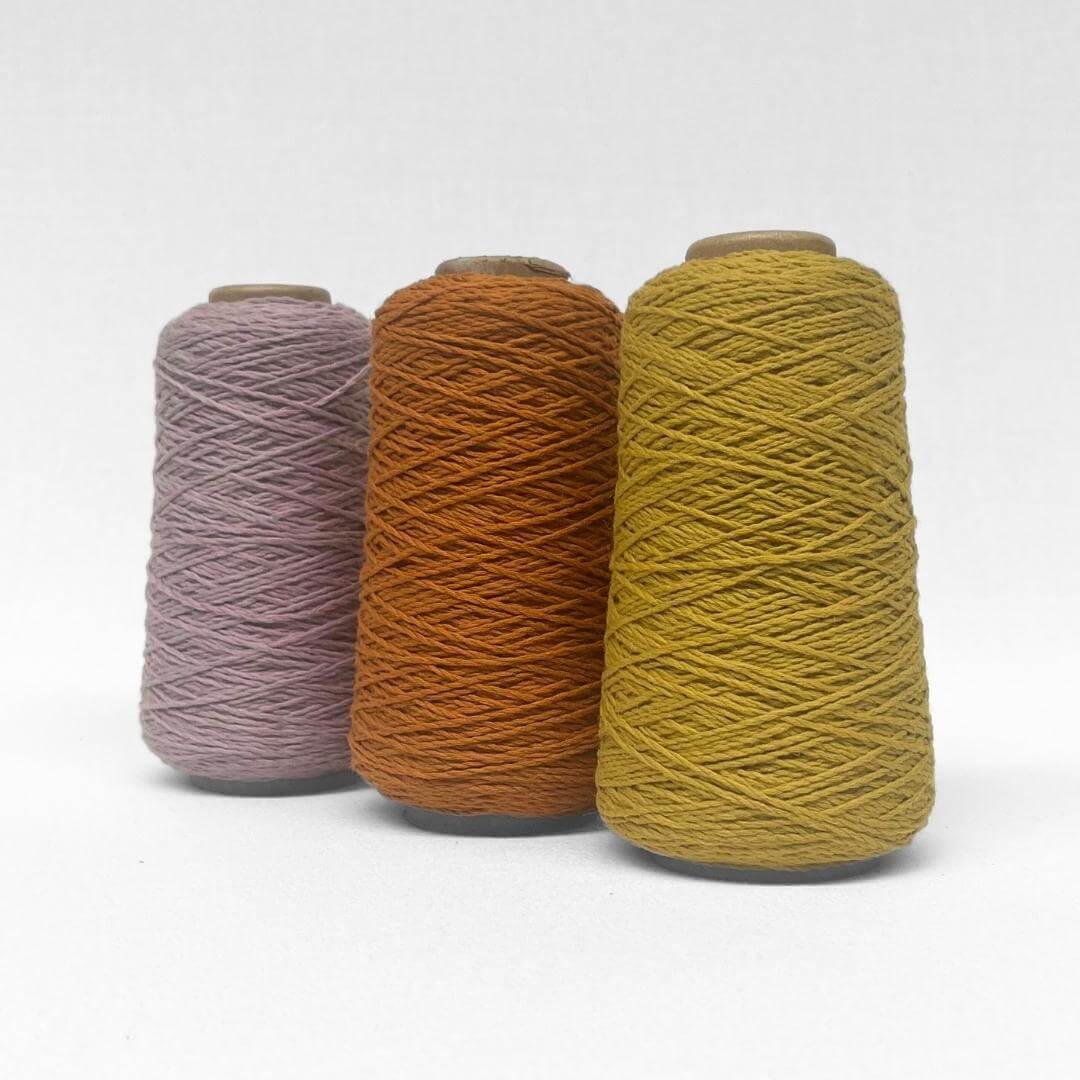 three rolls of wool yarn in mustard yellow and pink standing upright on white background