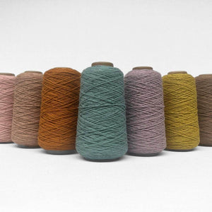 seven rolls of woollen yarn in different colours standing in triangle formation on white background