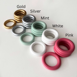 gold silver mint white and pink wooden craft rings stacked in tower on white desk